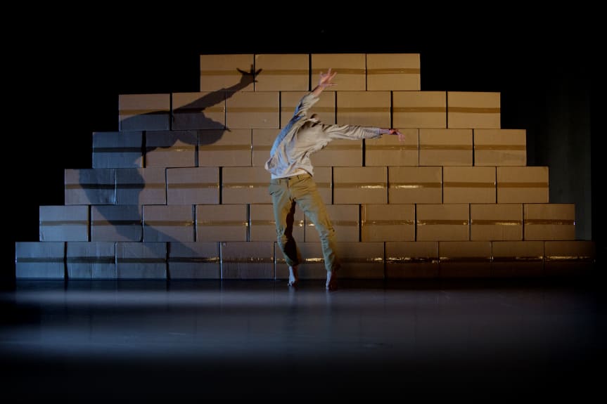 Dansare framför mur av kartonger.  Foto: Skåne Dansteater 
