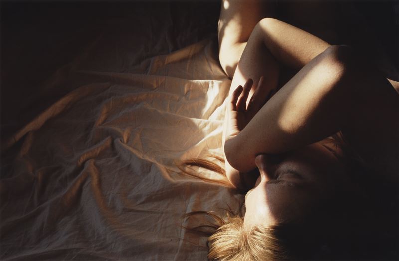 Kvinna ligger ihopkrupen på sängen. Fotograf: Lina Scheynius