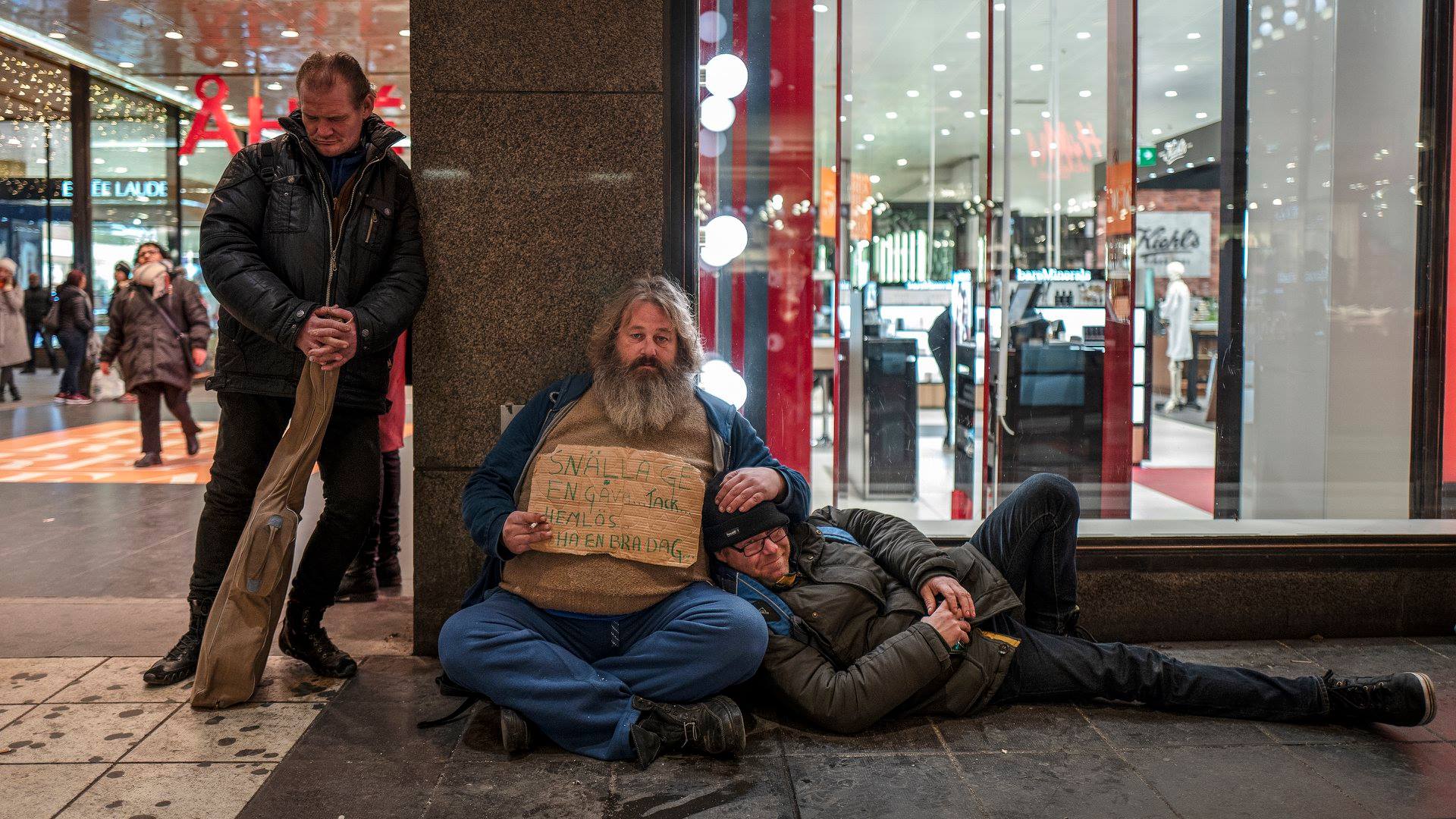 Tre hemlösa sitter, ligger o står utanför ett köpcentrum. Foto: SVT